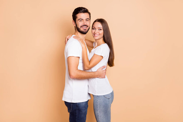 Zdjęcie cute ładny mąż żona nosić białe t-shirty obejmujące uśmiechnięty odizolowany beżowy kolor tła - Zdjęcie, obraz