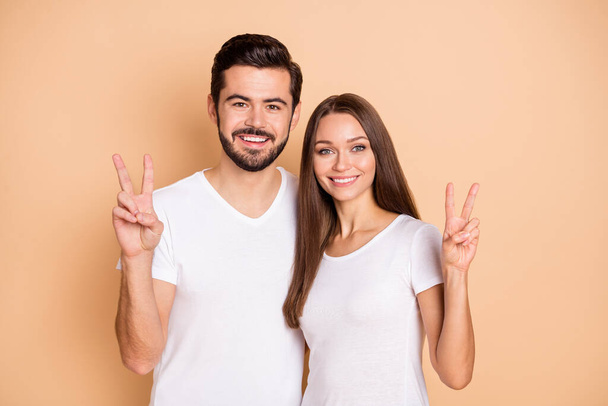 Photo of pretty sweet husband wife wear white t-shirts hugging showing v-sign isolated beige color background - Foto, Bild