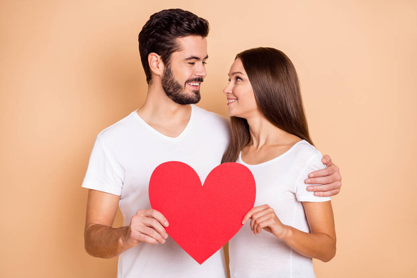 Photo of young lovely couple hug look each other hold big heart feelings love valentine day isolated over beige color background - Photo, image
