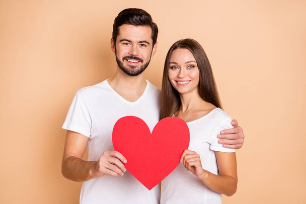Portrait of handsome guy pretty lady hug hands hold red paper heart card isolated on beige color background - Φωτογραφία, εικόνα