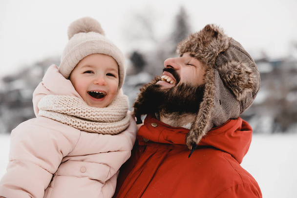 Genç şık sakallı baba ve küçük kızı kış tatilinde. Baba oğlunu parka geri götürüyor. Mutlu, neşeli bir aile. Mutlu, neşeli bir aile. - Fotoğraf, Görsel