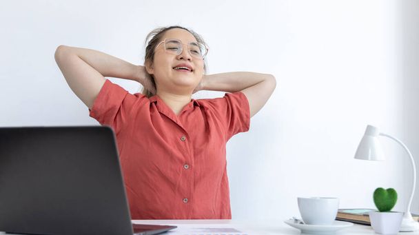 Joven empleada asiática está haciendo una postura relajante después de un duro trabajo de mediodía, mujeres felices descansando en el trabajo después de terminar el trabajo, la fatiga se alivia, las mujeres que trabajan en casa. - Foto, imagen