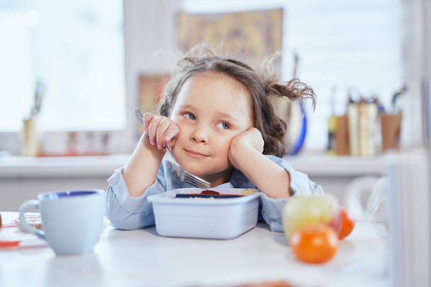 Χαριτωμένο μικρό κορίτσι τρώει νόστιμο γεύμα κάθεται στο τραπέζι - Φωτογραφία, εικόνα