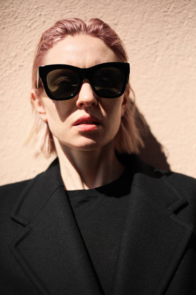 Young woman with pinkish hair, wearing sunglasses looking straight. - Valokuva, kuva