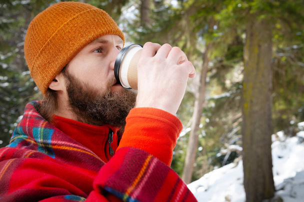bearded man drinking from a paper cup with a blanket on his shoulders - Foto, immagini