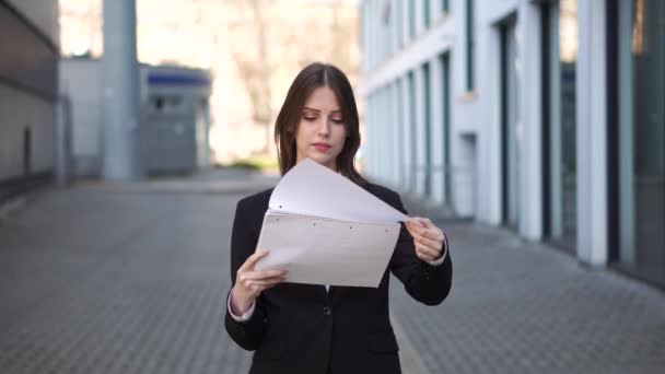 Een zelfverzekerde zakenvrouw staat buiten een business center en bladert door documenten. - Video
