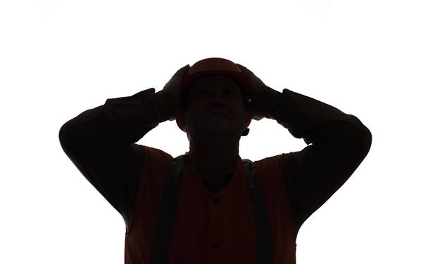 dark silhouette figure of contruction worker clutching head in helmet on white isilated background in stress, foreman worried about progress of work - Fotografie, Obrázek