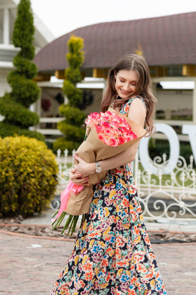 Boldog mosolygós lány egy csokor rózsával a kezében. Lenézett, vagy a csokorra. Egy nő ünnepli a születésnapját vagy más ünnep - Fotó, kép