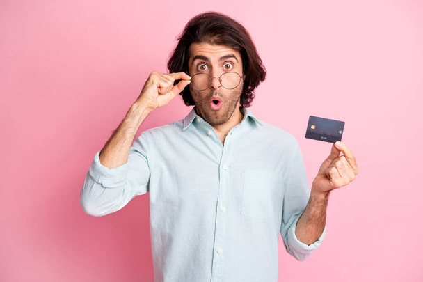 Portrait of young handsome shocked surprised man male guy hold credit card wear glasses isolated on pink color background - 写真・画像