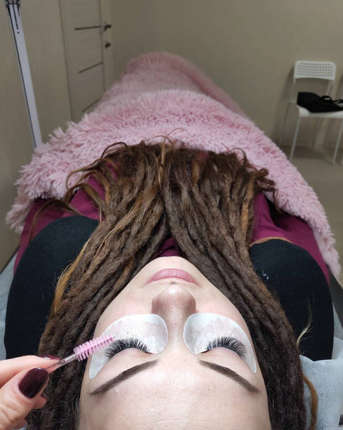 Femme avec dreadlocks dans le salon de beauté sur les extensions de cils  - Photo, image