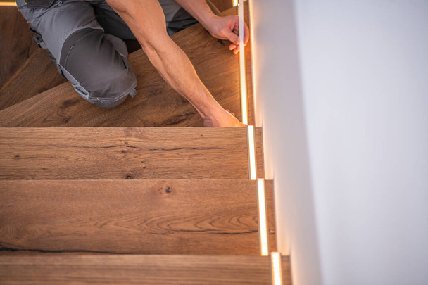 Installazione professionale di luci di scale in legno residenziale a LED per la finitura caucasica dei lavoratori. Tecnologie di illuminazione domestica moderna. - Foto, immagini