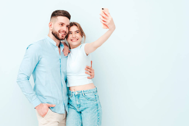 Smiling beautiful woman and her handsome boyfriend. Happy cheerful family having tender moments near light blue wall in studio.Pure cheerful models hugging.Embracing each other.Taking selfie - Foto, afbeelding