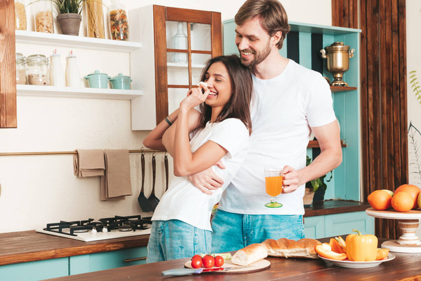 Smiling beautiful woman and her handsome boyfriend.Happy cheerful loving family having tender moments.Pure models making breakfast.Embracing each other.Cooking together in light kitchen at home - Zdjęcie, obraz