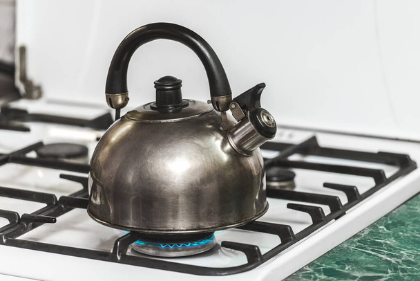 A metal dark kettle with a whistle heats the water to a boil on a gas stove in the kitchen. - Photo, Image