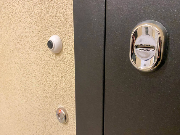 Nouvelle porte d'entrée en métal noir avec cloche et alarme de sécurité avec trou de serrure dans le couloir d'entrée. - Photo, image