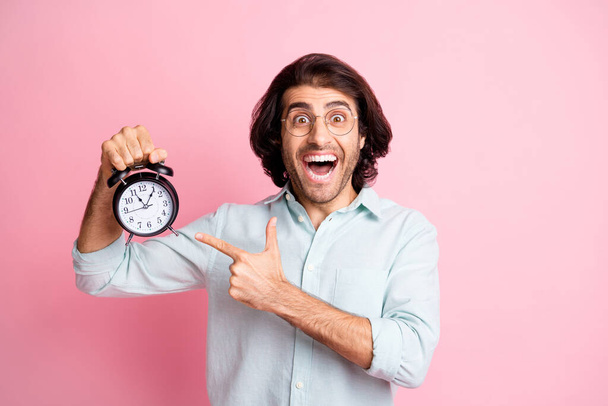 Photo of cheerful funny guy pointing clock wear spectacles blue shirt isolated on pastel pink color background - Foto, Imagem