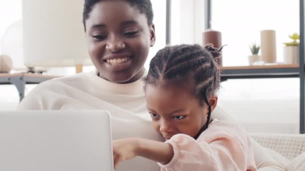 Portret afrykańska matka kobieta i afro amerykański czarny dziewczynka córka dziecko siedzi razem w domu patrząc w laptopie, dziecko wskazuje palcem na ekranie machając cześć, rodzina podejmowania rozmowy wideo online - Materiał filmowy, wideo