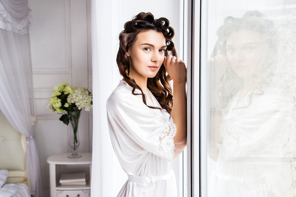 Beautiful bride in white silk lingerie in her bedroom near window in a morning - Фото, зображення