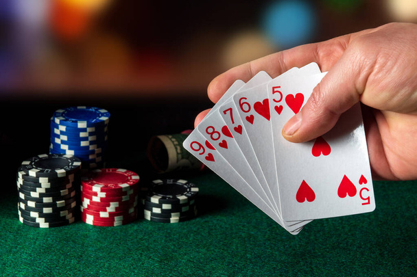  Cartes de poker avec combinaison flush droite dans le jeu. Gros plan d'une main de joueur tient des cartes à jouer dans le club de poker. Chips sur la table verte - Photo, image
