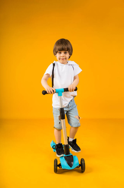 Neşeli küçük çocuk sarı bir arka planda scooter sürüyor ve mesaj için bir yeri var. Çocuklar için spor - Fotoğraf, Görsel