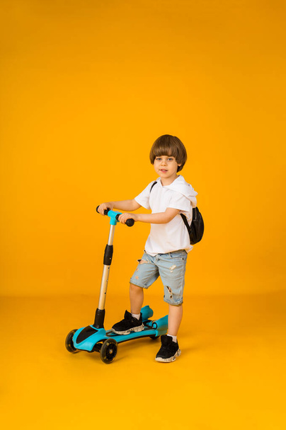 Küçük çocuk sarı arka planda scooterıyla duruyor ve mesaj için yer var. Çocuklar için spor - Fotoğraf, Görsel
