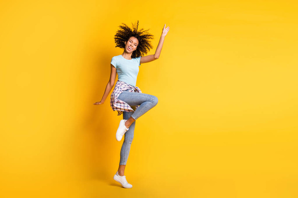 Full length photo of sweet shiny dark skin curly girl dressed blue t-shirt dancing empty space isolated yellow color background - Photo, Image