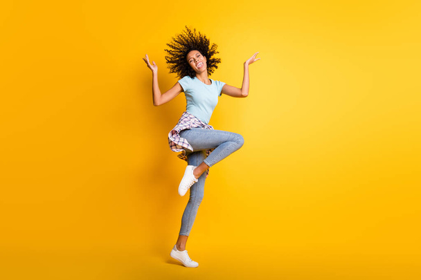 Full length photo of pretty cute shiny dark skin wavy lady wear blue t-shirt jumping rising arms hands isolated yellow color background - Foto, afbeelding