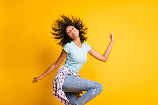 Photo of adorable pretty cute dark skin wavy lady wear blue t-shirt dancing isolated yellow color background - Foto, immagini