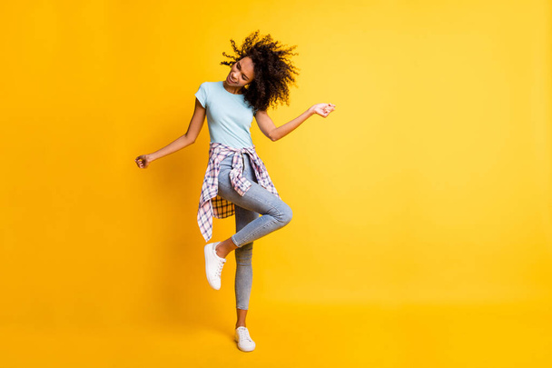 Full length photo of cute carefree dark skin curly girl dressed blue t-shirt dancing empty space isolated yellow color background - 写真・画像