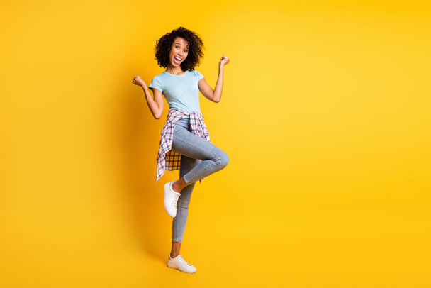 Full length photo of lucky dark skin curly woman dressed blue t-shirt rising fists empty space isolated yellow color background - Fotografie, Obrázek