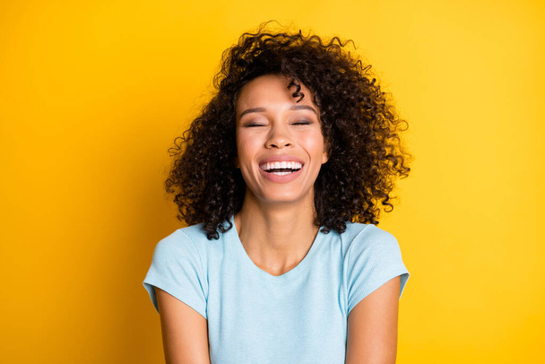 Photo of adorable funny dark skin curly woman dressed blue t-shirt laughing closed eyes isolated yellow color background - Φωτογραφία, εικόνα