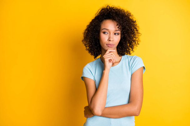 Photo of pretty serious dark skin wavy lady wear blue t-shirt arm chin looking empty space isolated yellow color background - 写真・画像