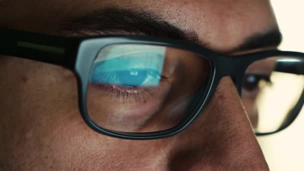 Macro en el ojo de un ingeniero de software que está trabajando: la mirada enfocada en la pantalla, en la lente de las gafas vemos el reflejo. Imagen clara y cristalina en la lente derecha. Enfoque selectivo - Metraje, vídeo