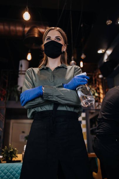 Young restaurant workers waiters cleaning and disinfecting tables and surfaces against Coronavirus pandemic disease. They are wearing protective face masks and gloves. - Zdjęcie, obraz