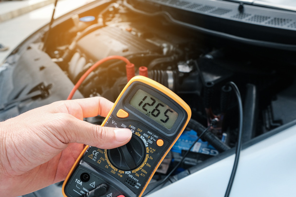 機械的な手は、車のバッテリーの電圧レベルを確認するためにマルチメータ電圧を使用します. - 写真・画像