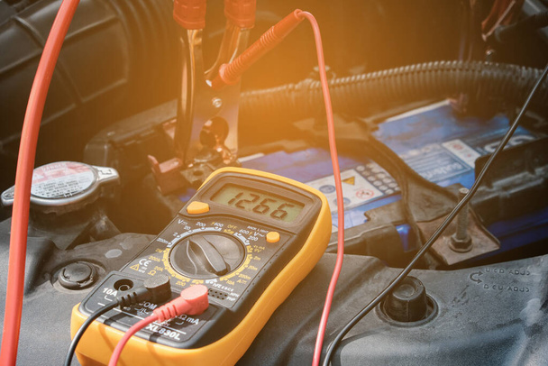 Mano mecánica utilice voltímetro multímetro para comprobar el nivel de voltaje en una batería de coche. - Foto, imagen