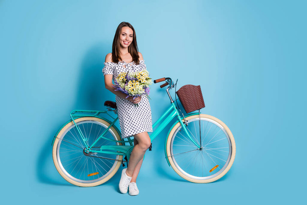 Full length photo of girl hold bouquet wildflowers look camera bike wear dotted short dress sneakers isolated blue color background - Foto, immagini