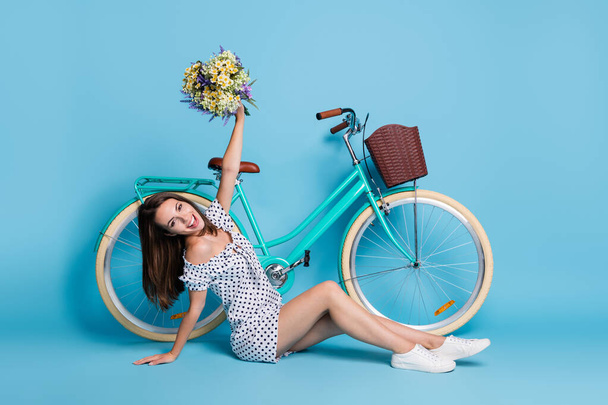 Full length photo of lady sit floor hold bunch flower bicycle look camera wear dotted mini dress footwear isolated blue color background - Foto, immagini