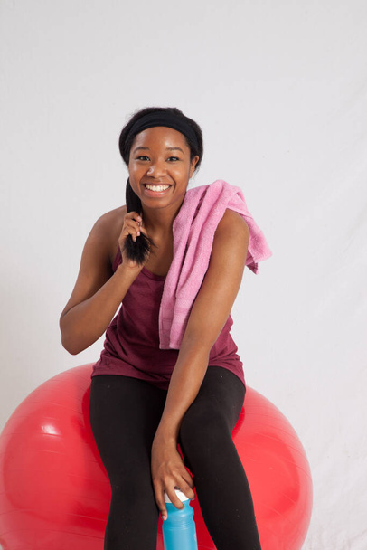 Preciosa mujer negra sentada en una pelota de ejercicio roja - Foto, imagen