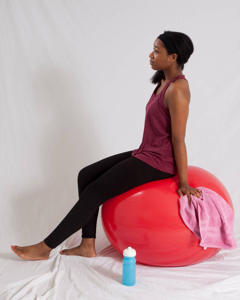 thoughtful black woman sitting on a red exercise ball - Fotoğraf, Görsel