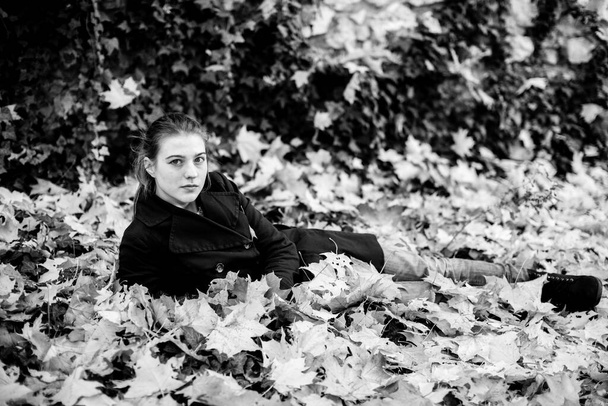 Nuori viehättävä tyttö makaa syksyn kaatuneissa lehdissä. Musta ja valkoinen kuva. - Valokuva, kuva