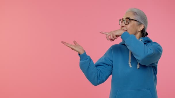 Anciana anciana abuela mostrando pulgares hacia arriba y apuntando a la izquierda en el espacio en blanco, logotipo de la publicidad - Imágenes, Vídeo