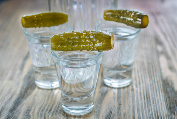Vodka dans un verre et concombre mariné. Boisson alcoolisée russe traditionnelle avec une collation - Photo, image