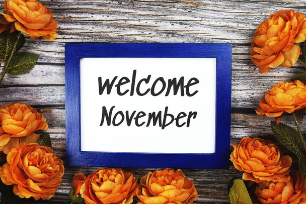 Welcome November text in blue border frame with flower decoration on wooden background - Foto, afbeelding