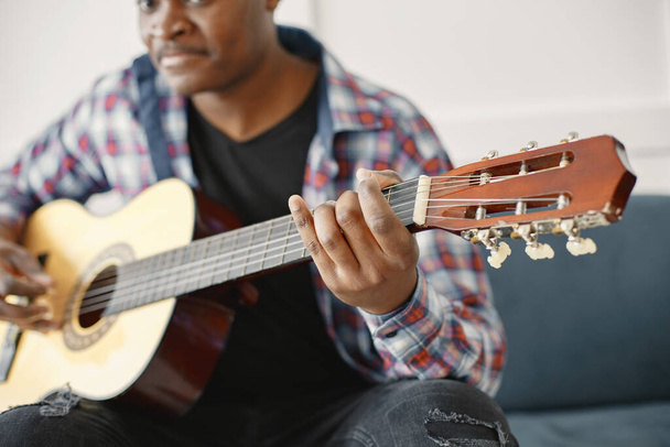 African man playing guitar while sitting on sofa - 写真・画像