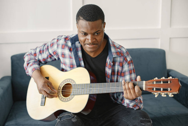 African man playing guitar while sitting on sofa - Photo, Image