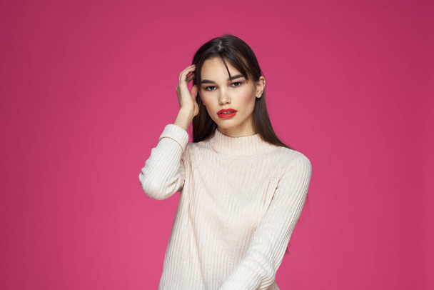Brunette with long hair red lips cosmetics white sweater pink background cropped view - 写真・画像