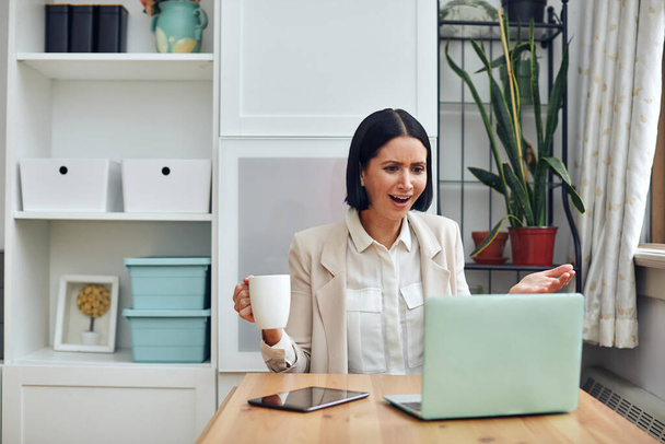 молодая красивая женщина с ноутбуком и чашкой кофе на столе в офисе - Фото, изображение