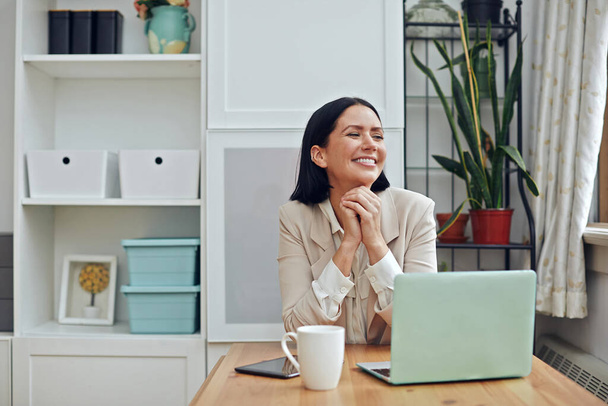 portrait d'une jeune belle femme avec ordinateur portable et tasse de café sur la tête et souriant tout en travaillant sur - Photo, image