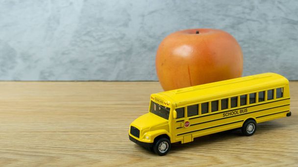 Schulbus-Spielzeug und Apfel auf Holztisch für den Schul- oder Ausbildungsweg - Foto, Bild